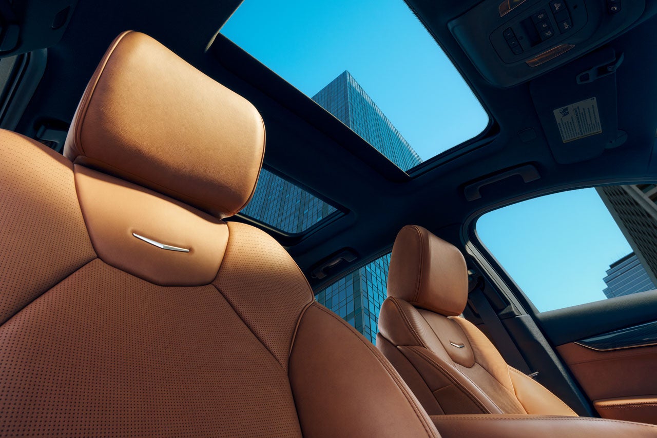 View from inside a car with a sunroof, showing brown leather seats and city buildings against a blue sky.