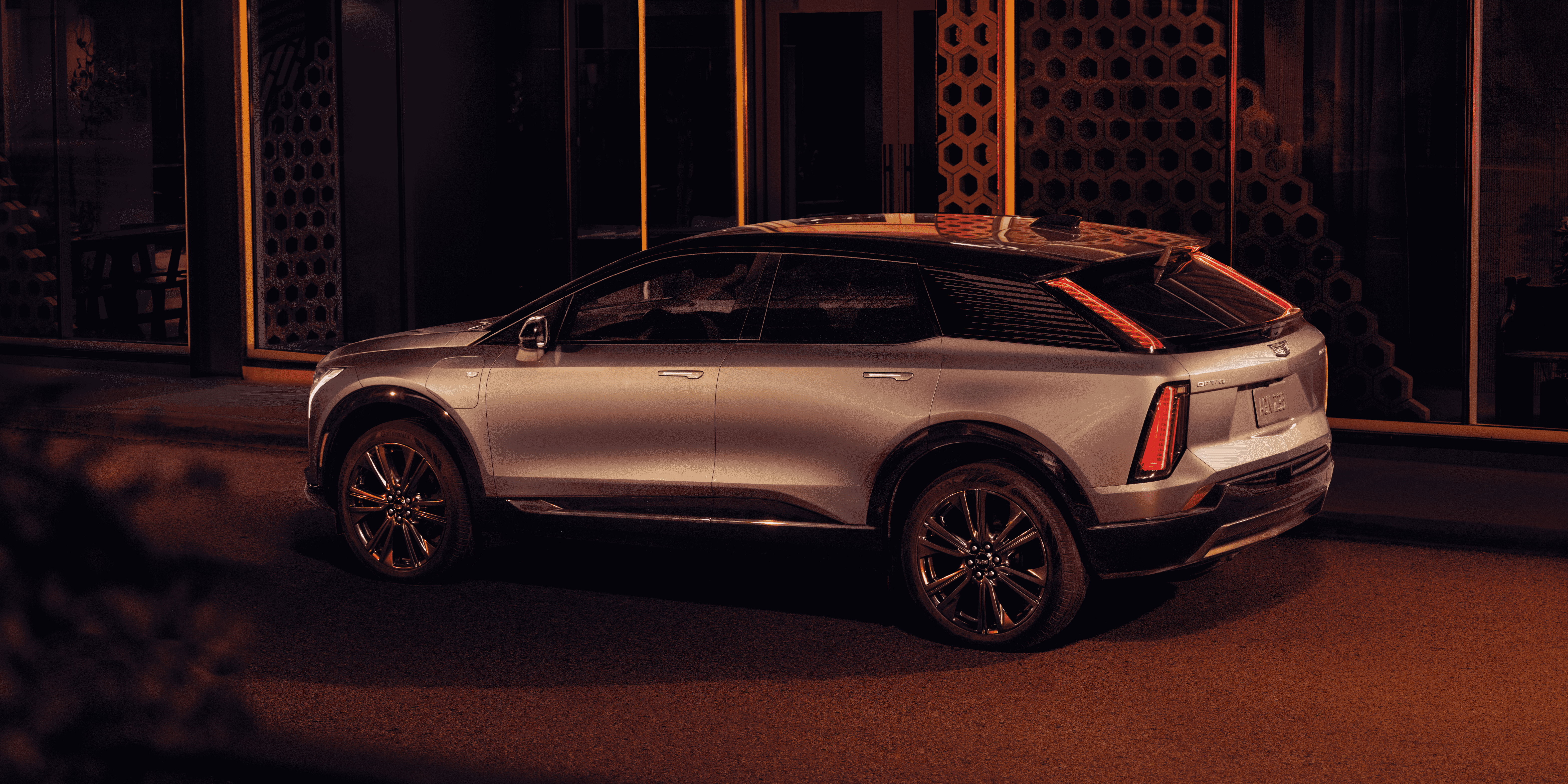 Silver Cadillac Optiq electric SUV parked on a city street at night with warm lighting.