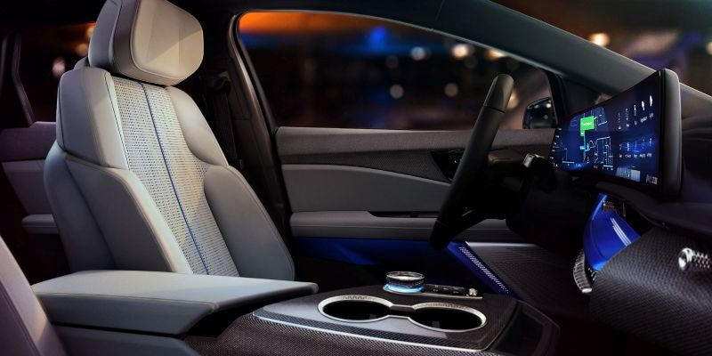 Orange Cadillac electric SUV parked in front of modern glass building.